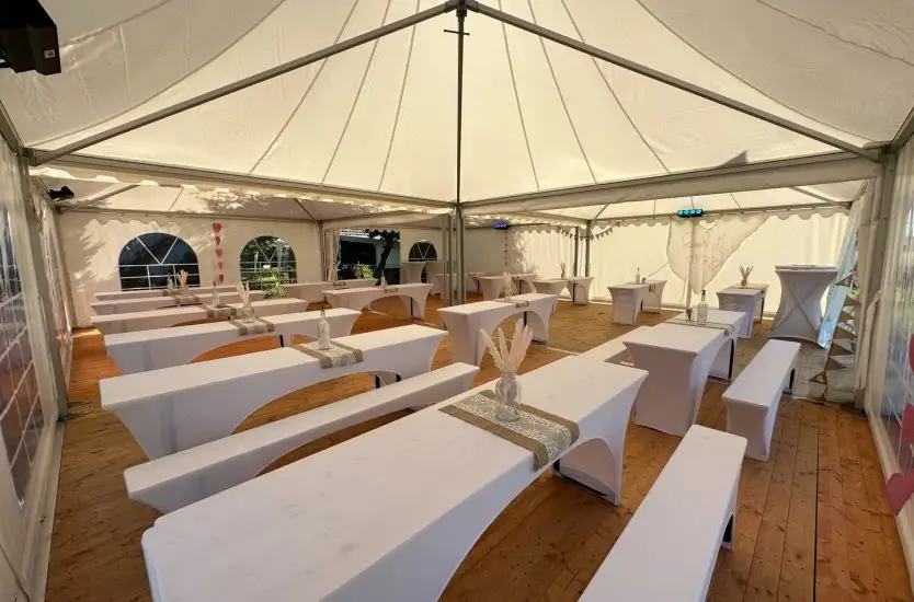 Clear span interior of an aluminum frame event tent with tables and wooden floor.