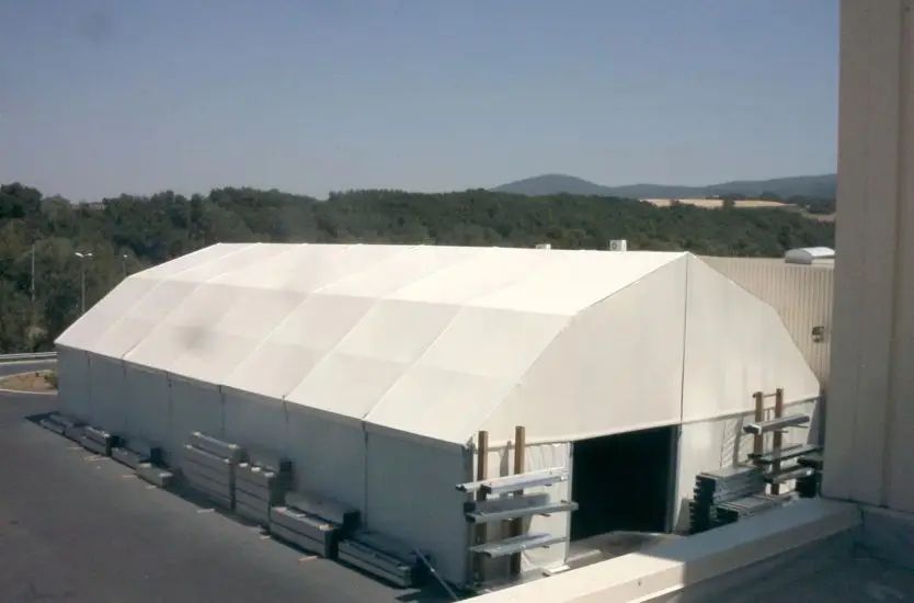 Heavy-duty polygonal warehouse tent used for industrial storage next to a building.