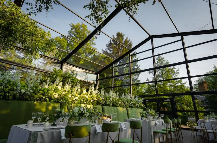 Interior of a black frame transparent clear span tent decorated with greenery for a formal dinner.