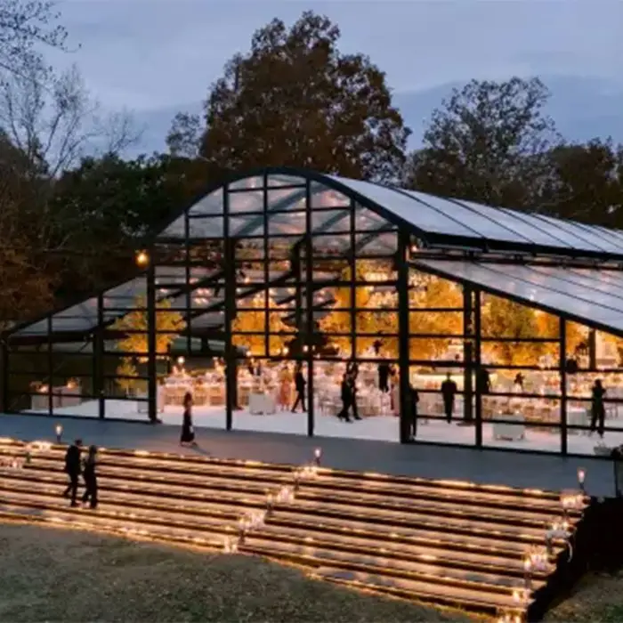 Large curved-roof black aluminum clear span tent glowing at dusk for an upscale outdoor event.
