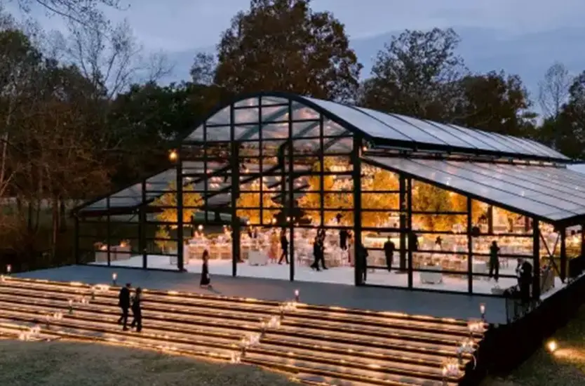 Large curved-roof black aluminum clear span tent glowing at dusk for an upscale outdoor event.