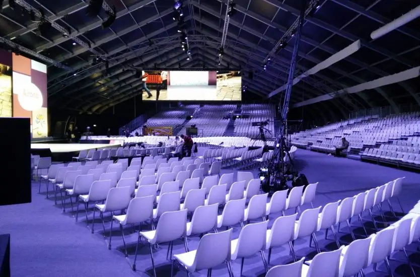 Massive clear span aluminum tent interior set up with tiered seating for a large conference.