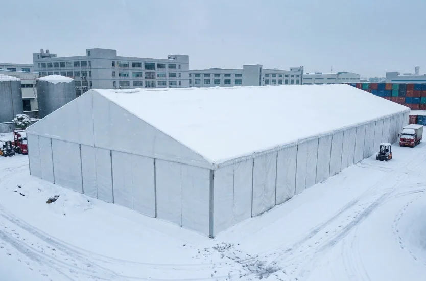 Large aluminum clear span warehouse tent covered in thick snow in an industrial park setting.